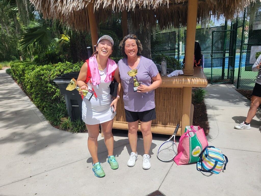 Ke (left) and a teammate laughing with their trophies outside the courts